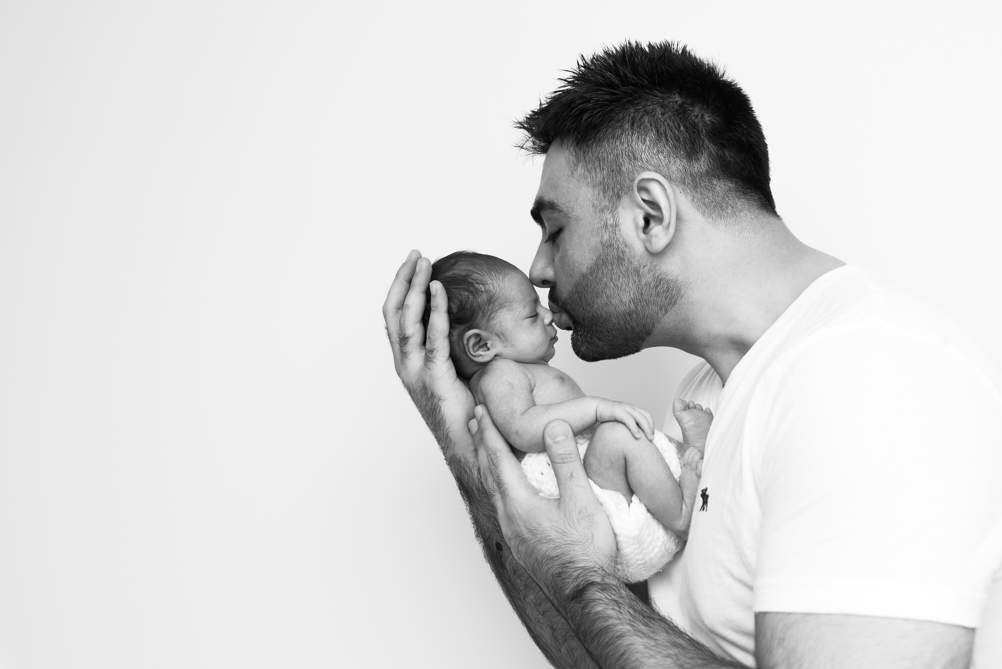 Black and white image of dad kissing baby by Clapham newborn photographer in South London