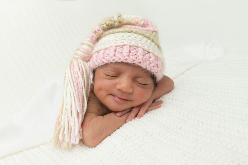 Smiling baby in pink hat taken at at-home newborn photography shoot in Fulham, West London